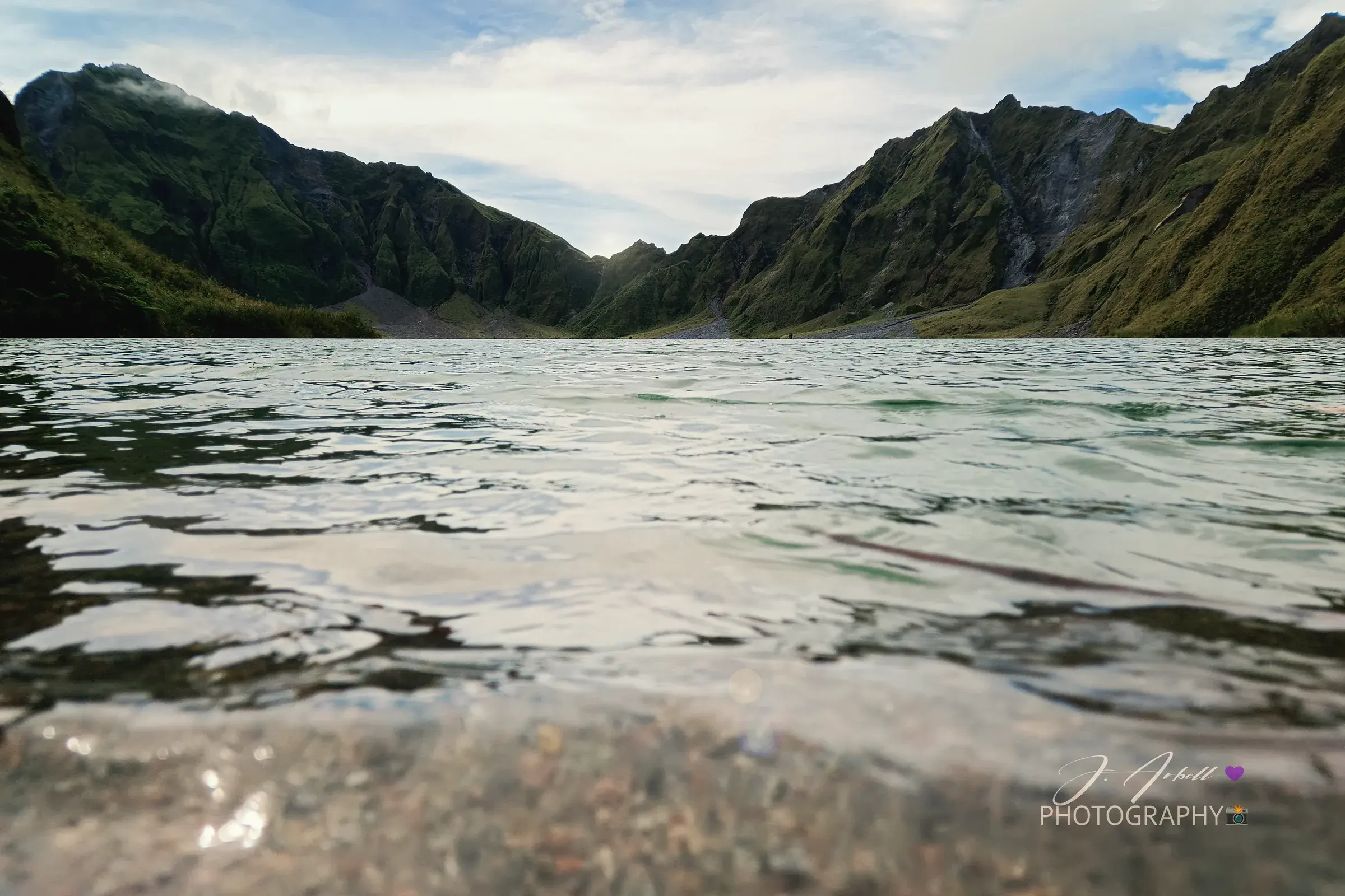 The crater lake of Mount Pinatubo photographed from water level, ridged green peaks enclosing the far shore