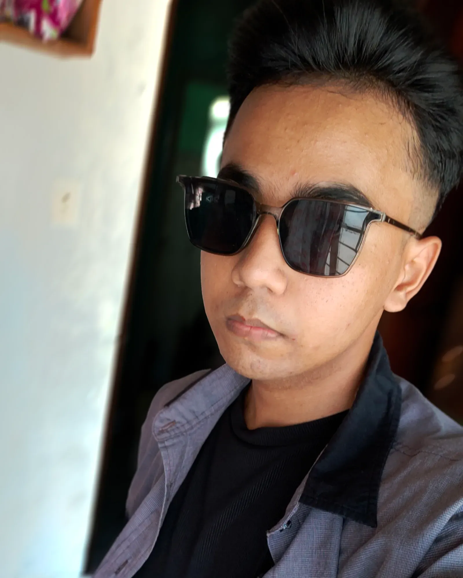 Jon Arbell in dark sunglasses and a grey button-up, lit by a sunlit doorway.