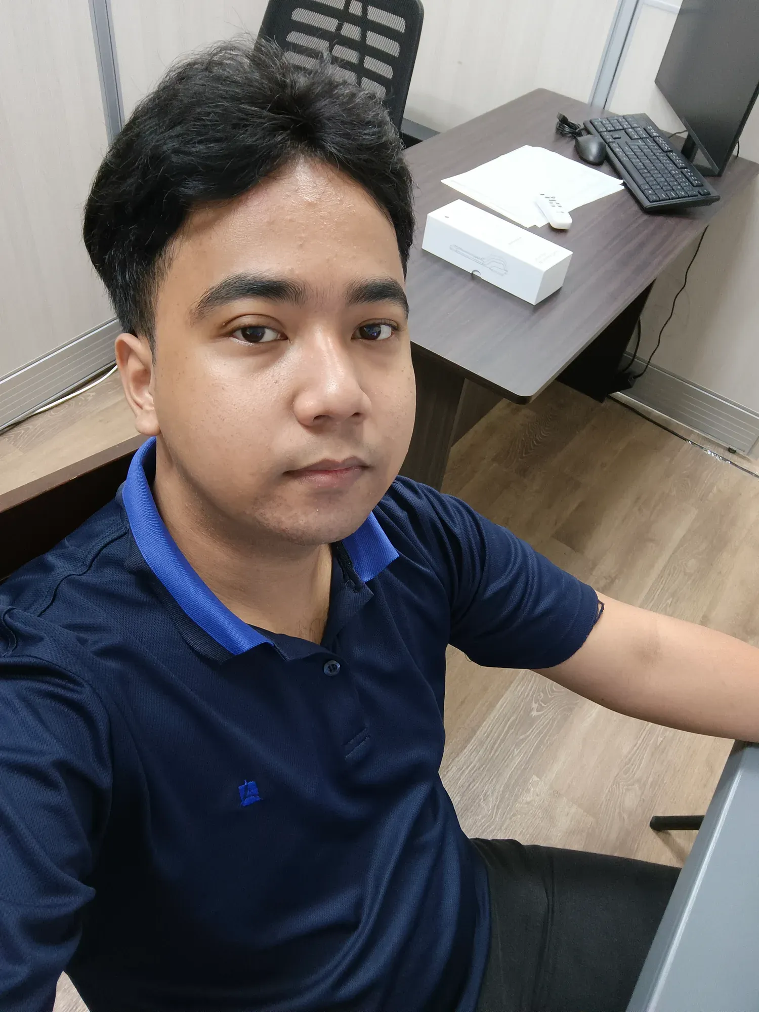 Jon Arbell at his office desk in a navy polo, workstation and monitor behind him.