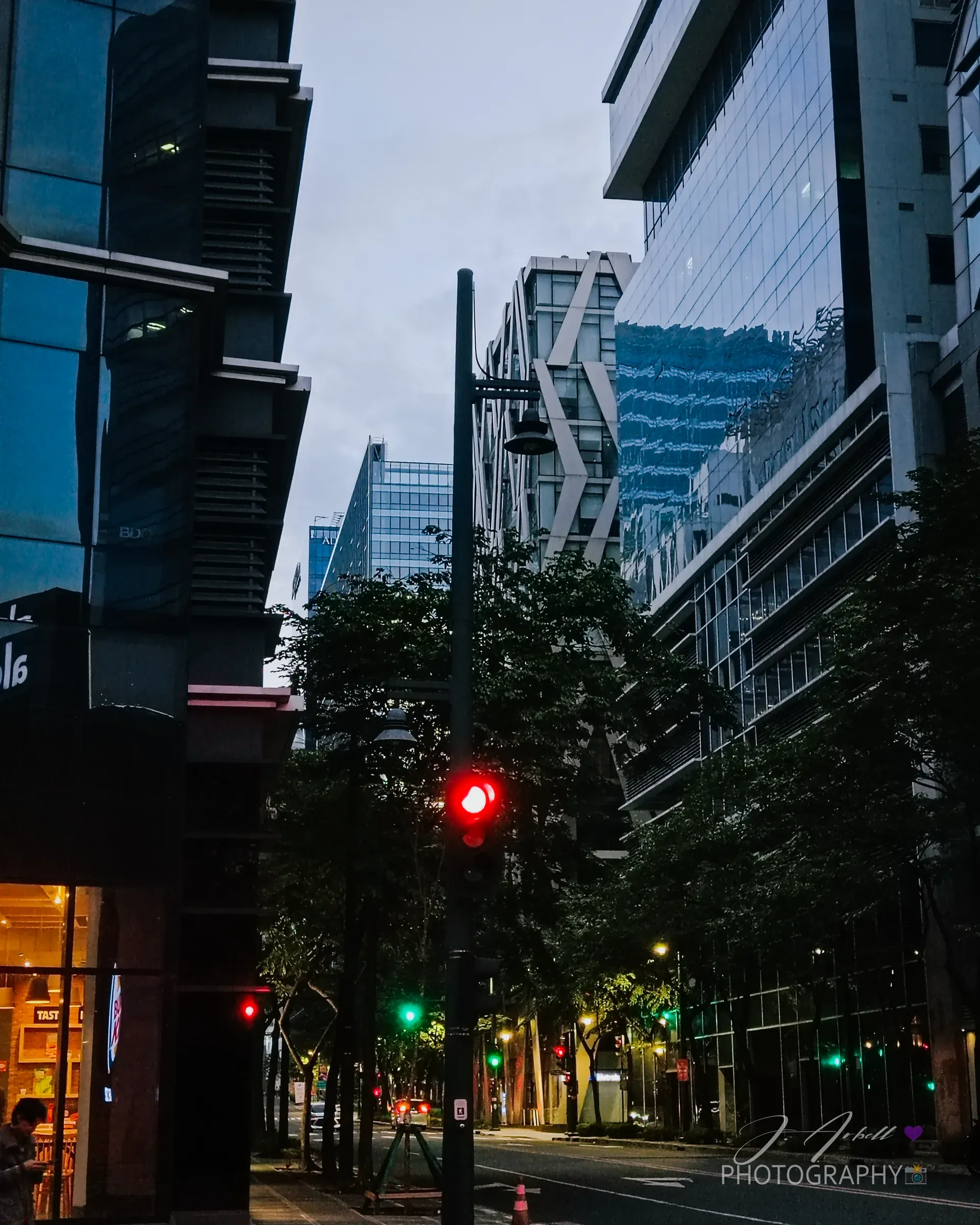 A BGC side street at blue hour, a red traffic light glowing between dark glass high-rises