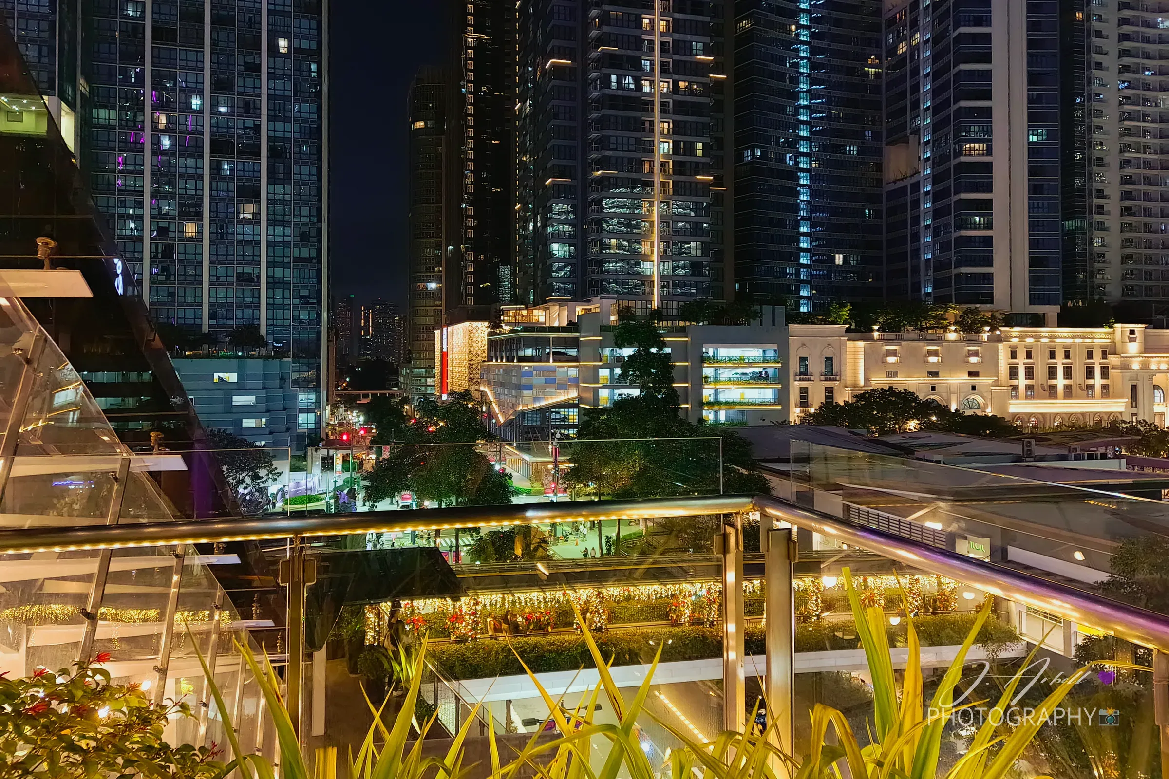 Bonifacio Global City at night seen from a planted rooftop terrace, lit residential towers filling the skyline