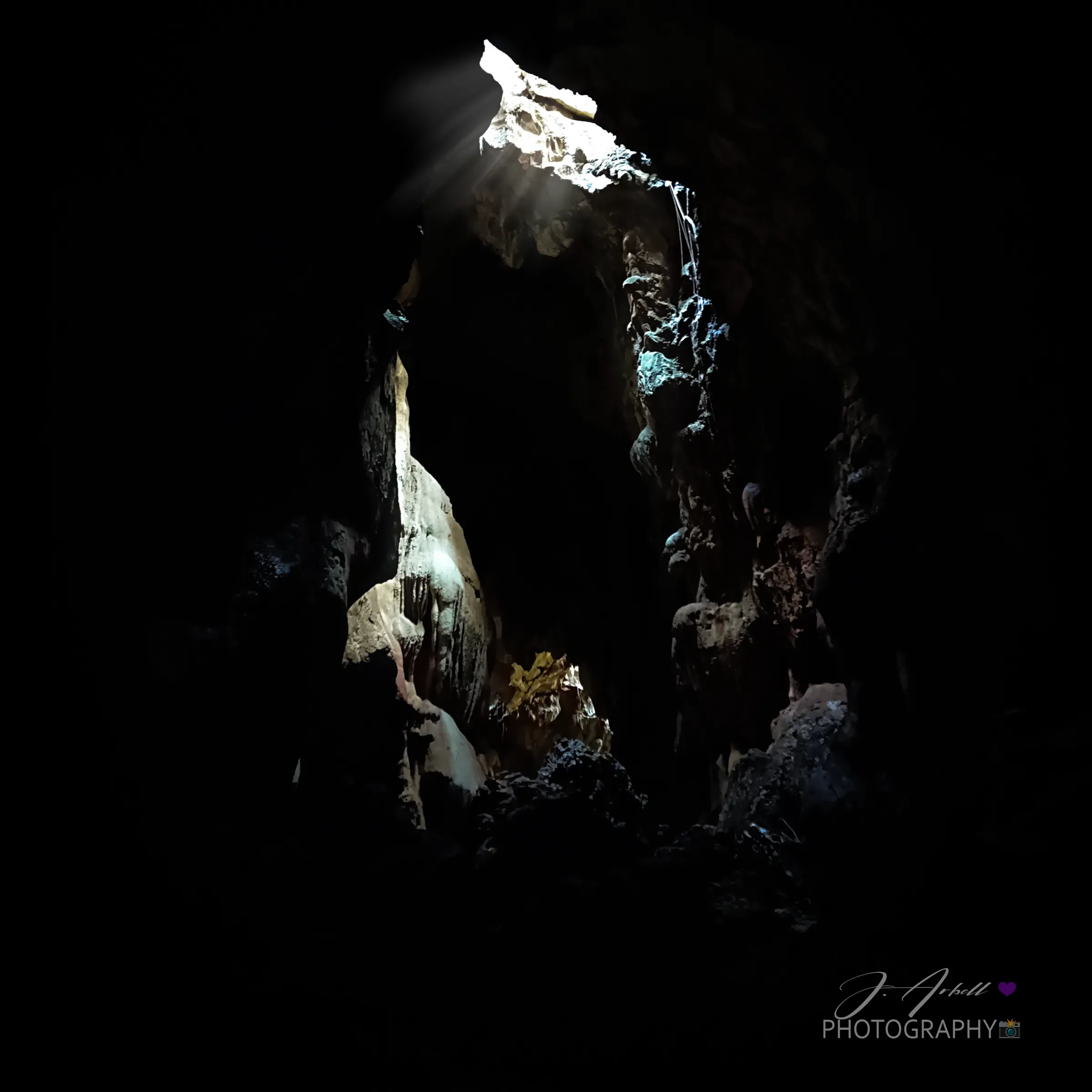 A shaft of daylight falling through an opening in the roof of Calinawan Cave onto pale limestone formations, the rest of the chamber in darkness