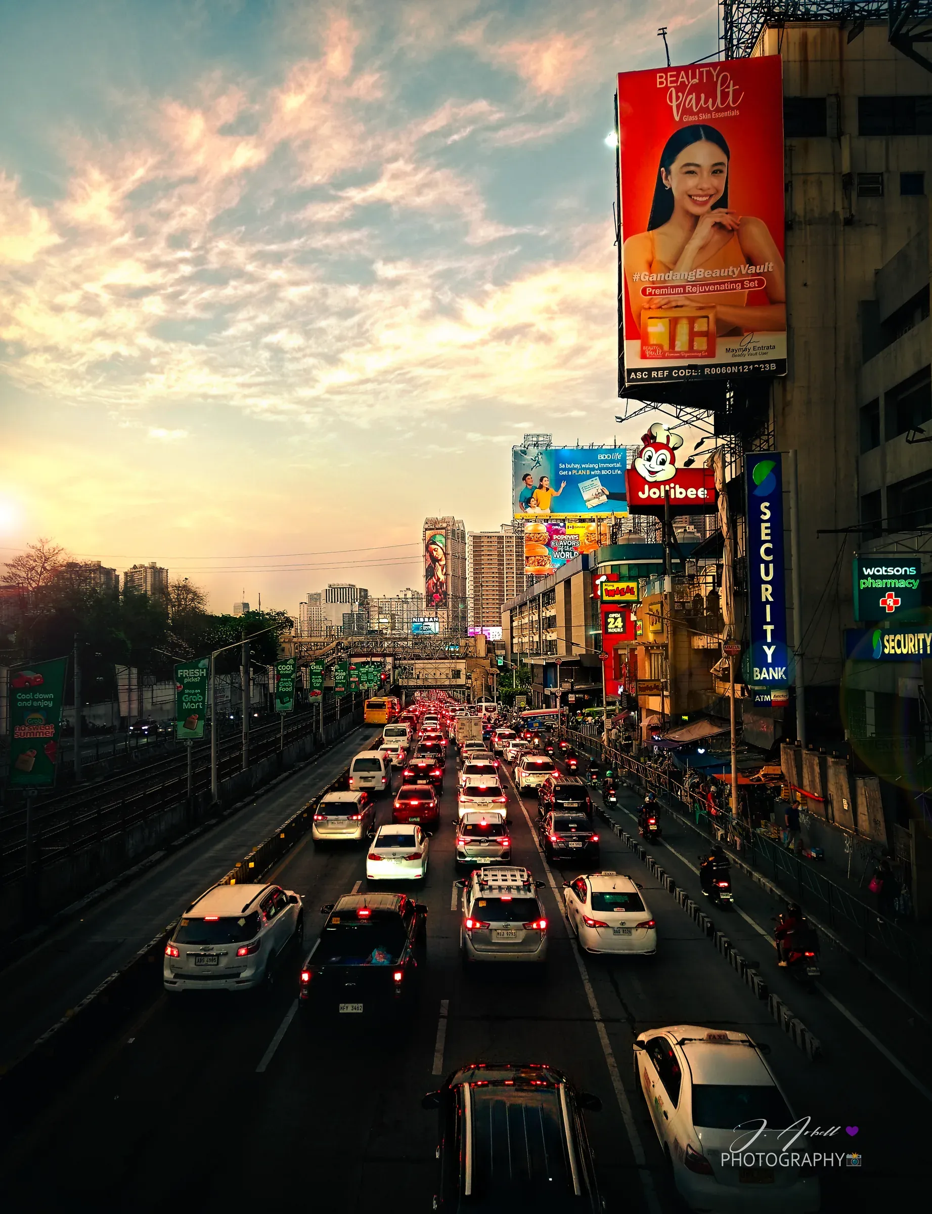 EDSA at Guadalupe seen from a footbridge at sunset, traffic queued in both directions beneath lit billboards and shopfront signs