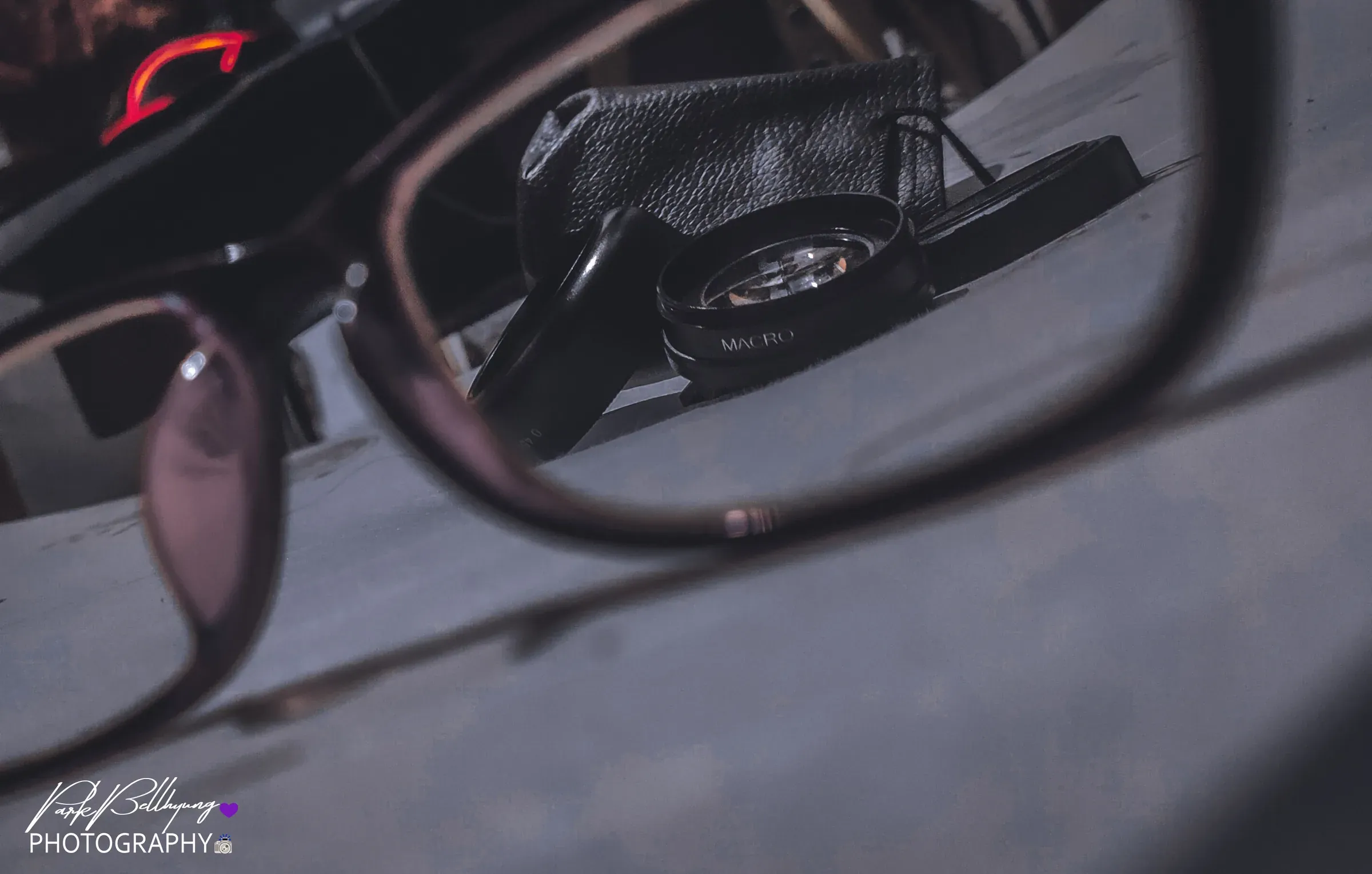 A clip-on macro phone lens and its leather pouch on a table, seen through the lens of a pair of eyeglasses in the foreground