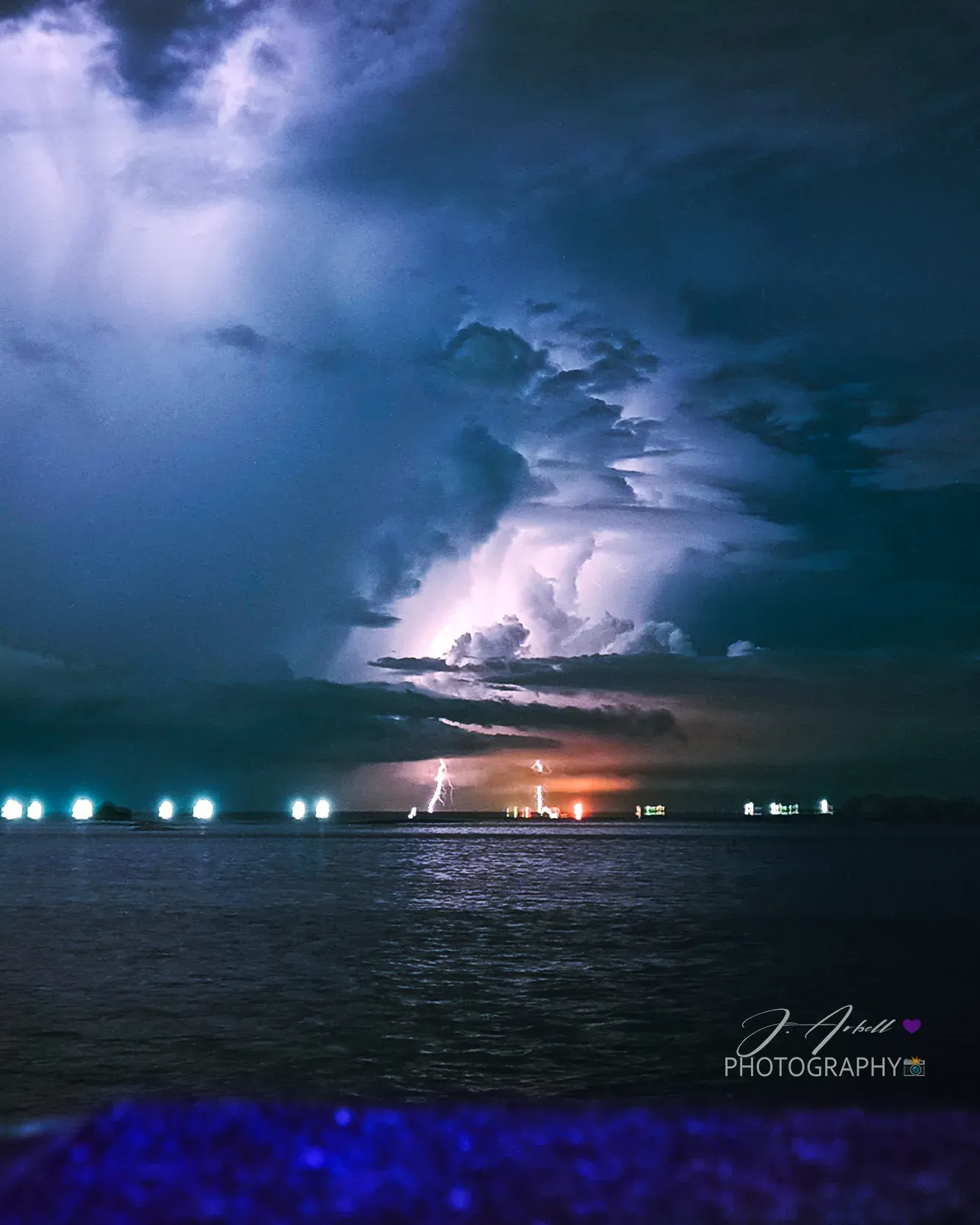 A thunderstorm over Manila Bay at night, forks of lightning striking behind a lit shoreline