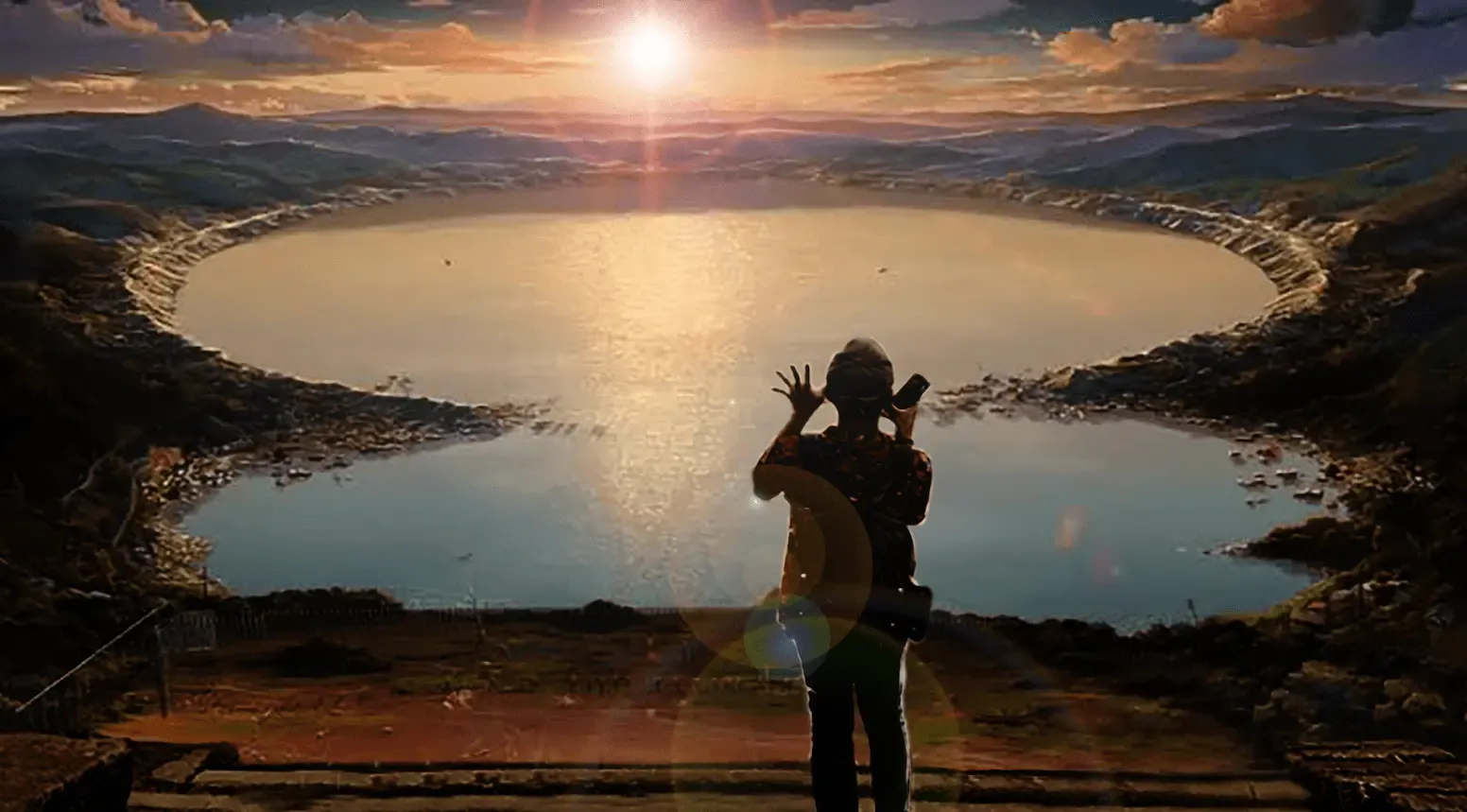 A photographer silhouetted against the sun setting over a crater lake, framing the shot on a phone