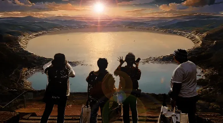 Four silhouetted figures on a ridge looking across a crater lake as the sun breaks over the far rim