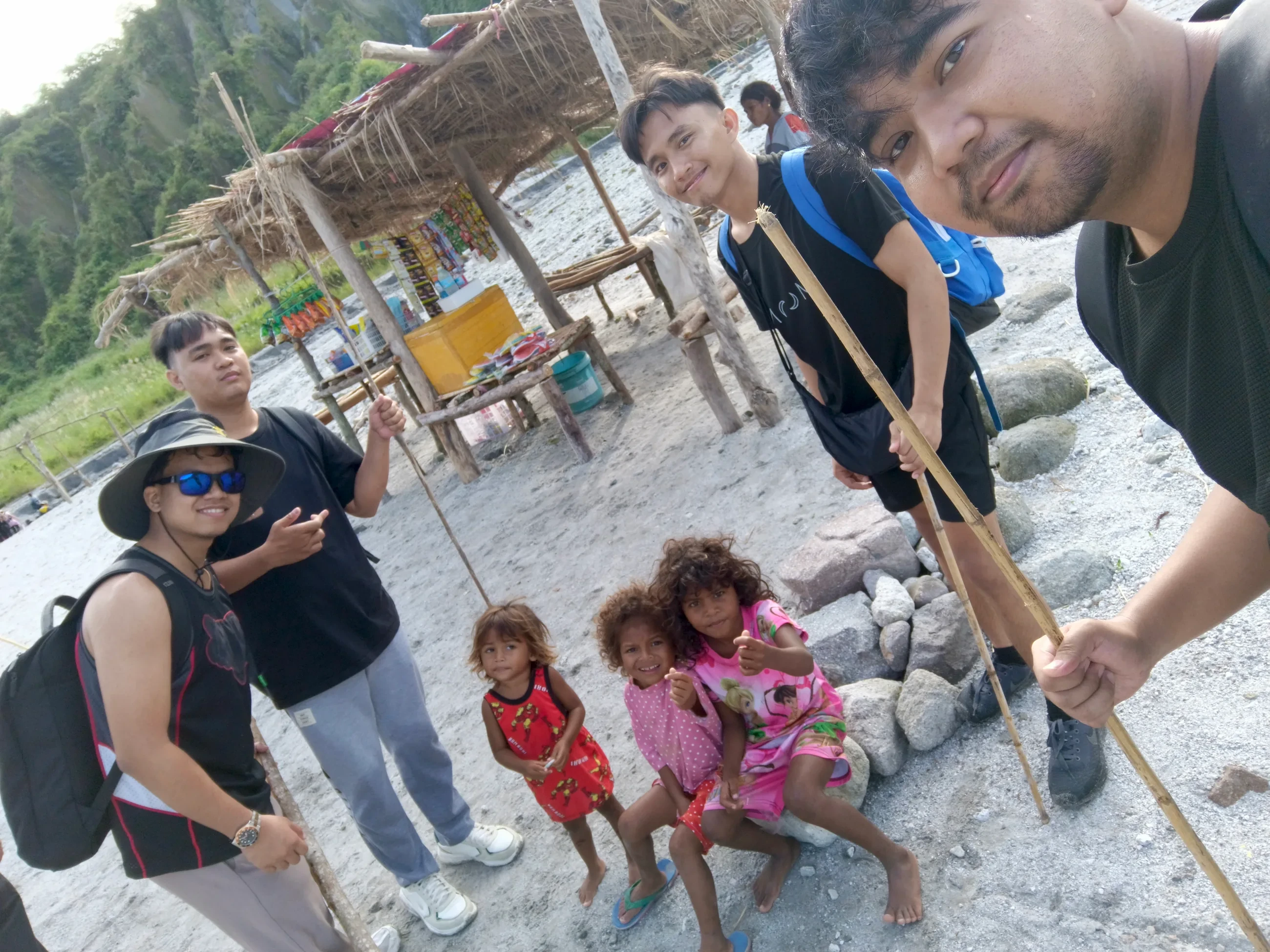 Jon Arbell and three friends on a Mt. Pinatubo trek, bamboo walking poles in hand, gathered with local children on the volcanic sand.